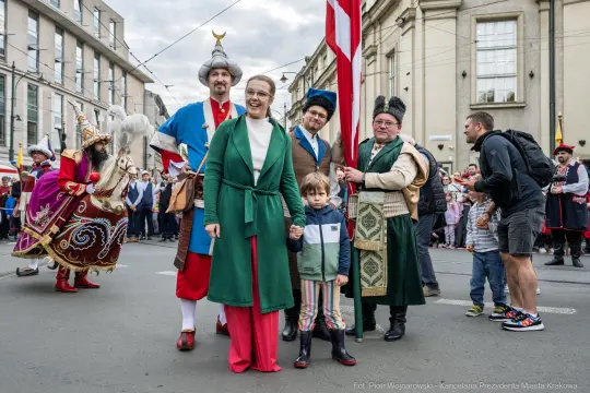 Parada z uczestnikami w tradycyjnych strojach, rodzina z dzieckiem na pierwszym planie.