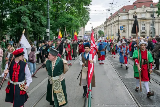 Parada z tradycyjnymi strojami, flagami i uczestnikami w historycznych kostiumach.