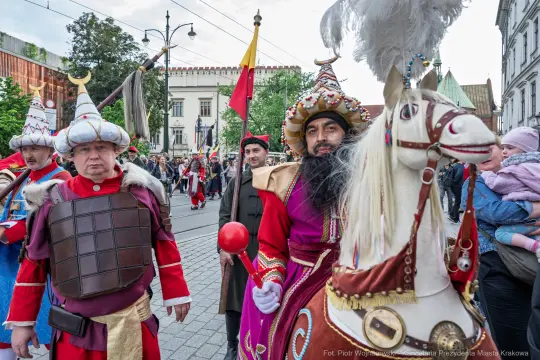Mężczyźni w kolorowych strojach historycznych, jeden z nich na koniu.