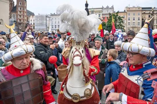 Uczestnicy parady w strojach historycznych z koniem w centrum miasta.