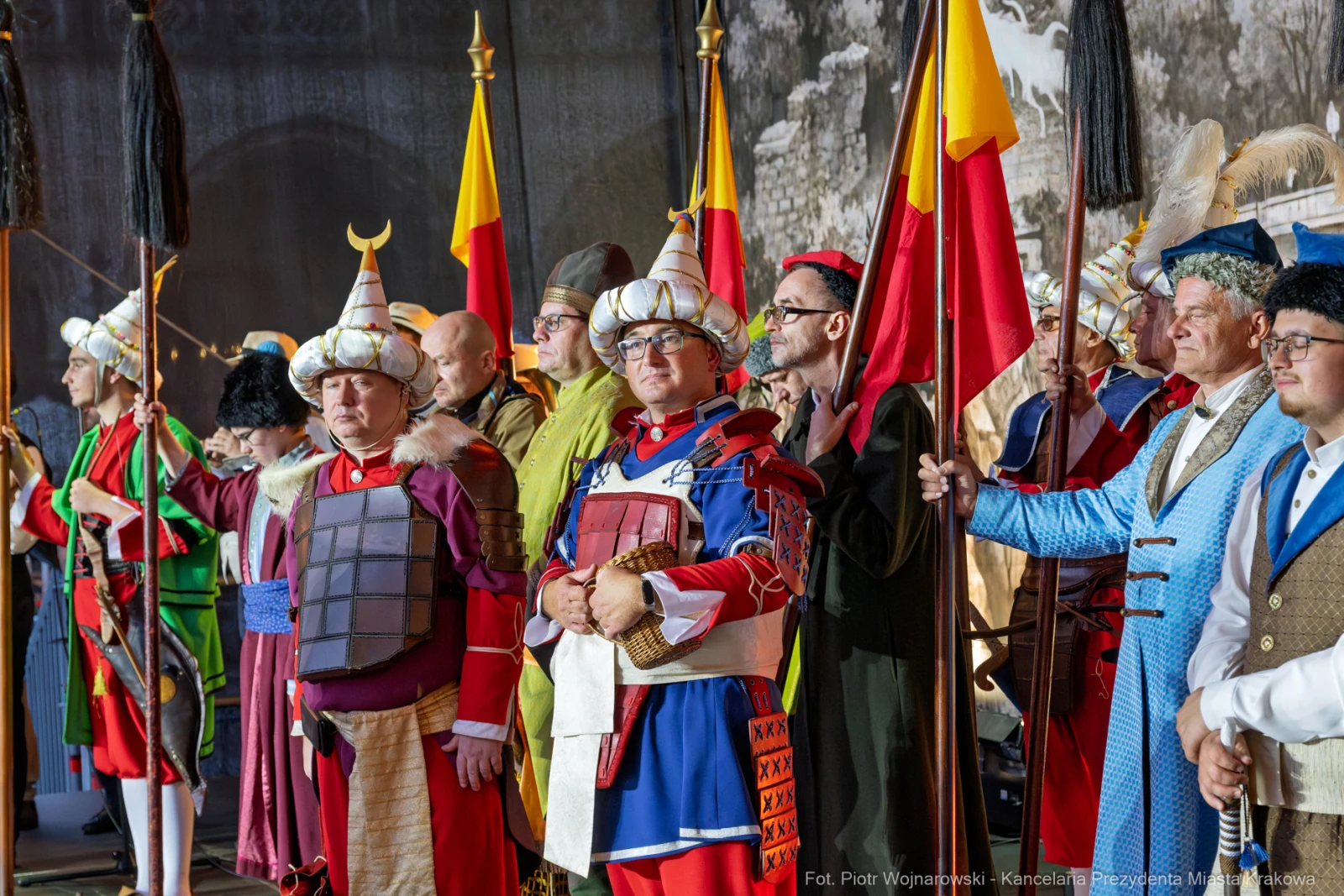 Grupa osób w historycznych strojach, trzymających flagi i broń, podczas wydarzenia kulturalnego.  Autor: Piotr Wojnarowski