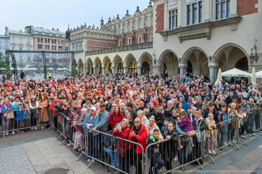 Tłum ludzi zgromadzony na rynku w Krakowie, z różnorodnymi emocjami i ubraniami.