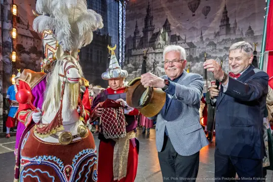 Mężczyźni w eleganckich strojach biorą udział w tradycyjnym występie z postacią w kostiumie.