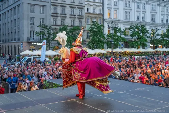 Artysta w kolorowym kostiumie tańczy na scenie przed tłumem widzów.