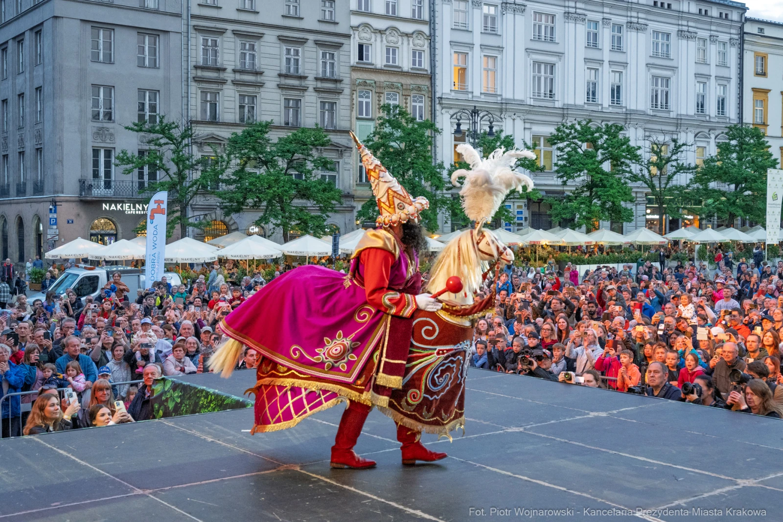 Kostiumowany artysta w kolorowej szacie tańczy na scenie przed tłumem ludzi.  Autor: Piotr Wojnarowski