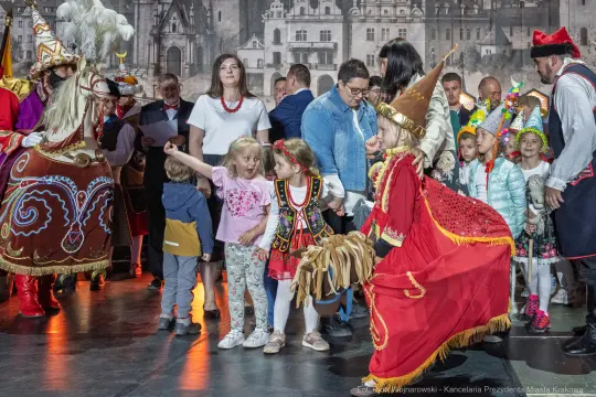 Grupa dzieci i dorosłych w tradycyjnych strojach, uczestniczących w wydarzeniu kulturalnym.