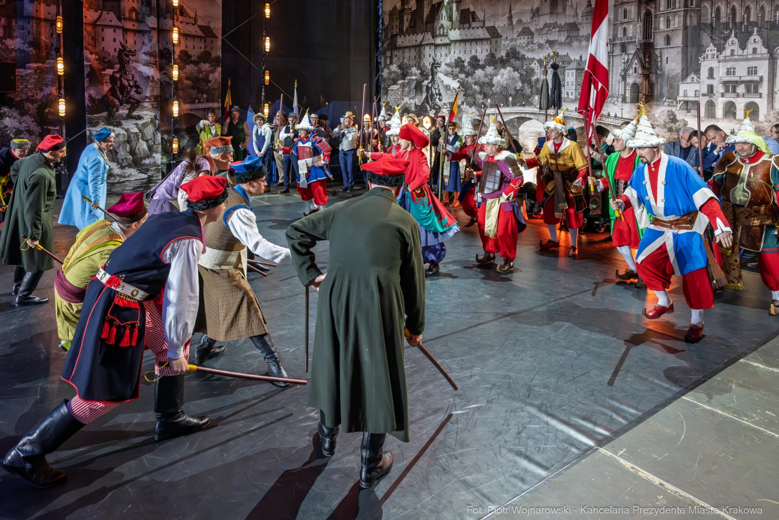 Scena z przedstawienia teatralnego z postaciami w historycznych strojach, tańczących i trzymających broń.  Autor: Piotr Wojnarowski