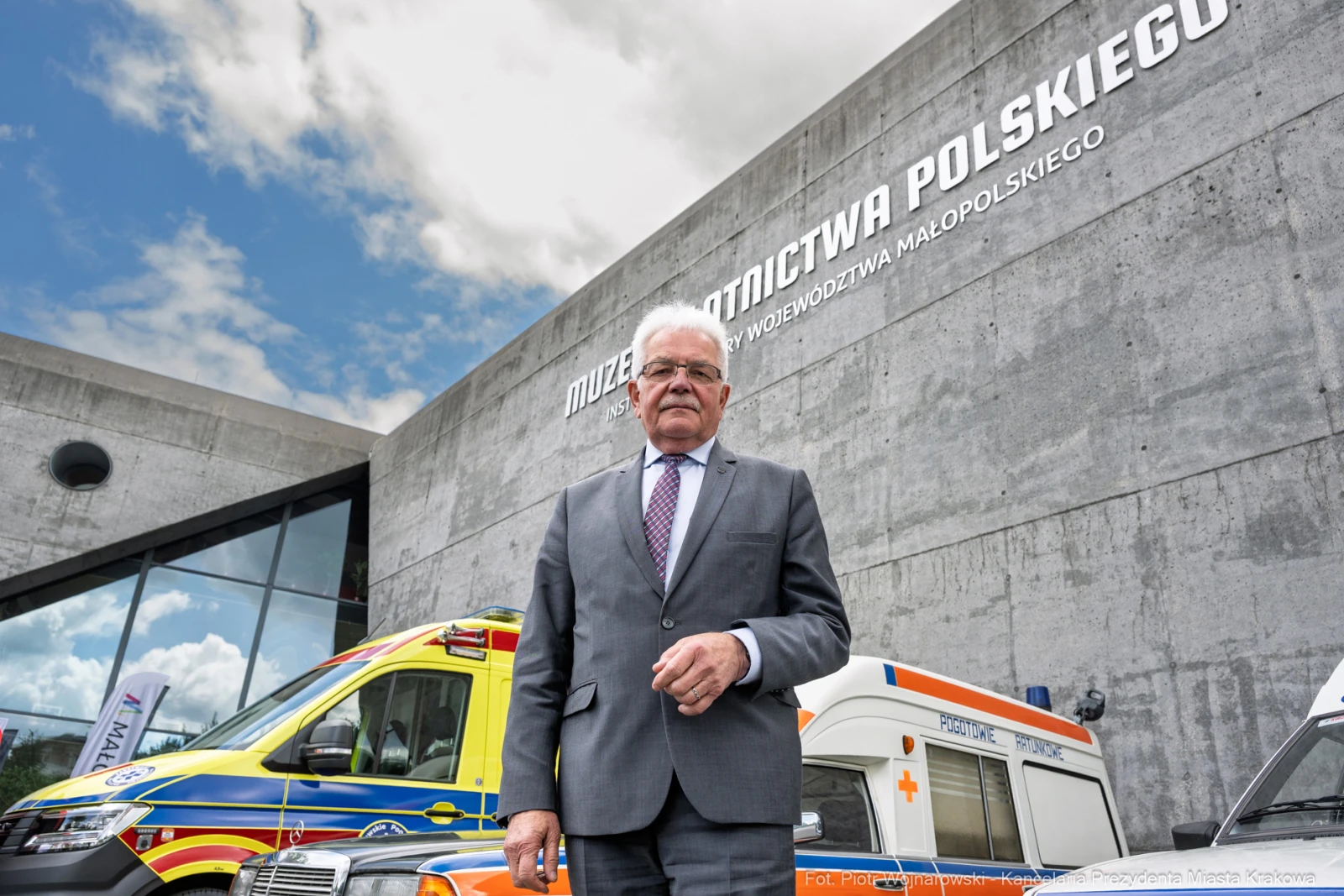 Mężczyzna w garniturze stoi przed nowoczesnym budynkiem muzeum z pojazdami ratunkowymi.  Autor: Piotr Wojnarowski