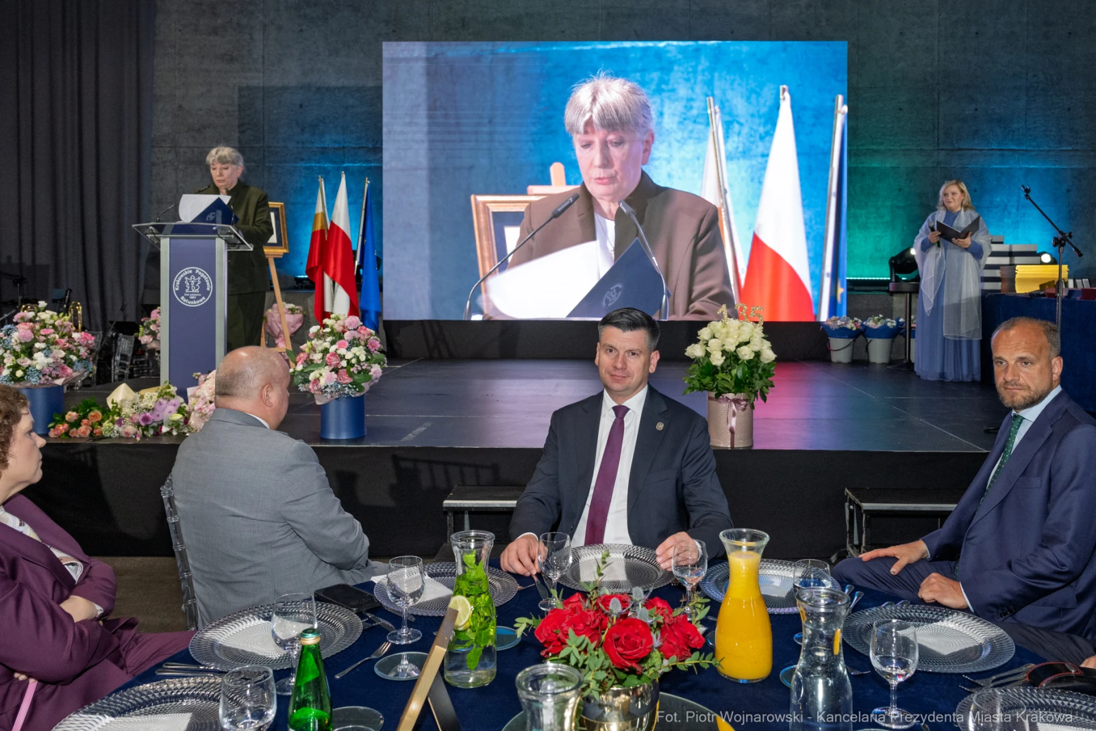 Uroczystość z przemówieniem, goście przy stole, ekran z prezentacją.  Autor: Piotr Wojnarowski