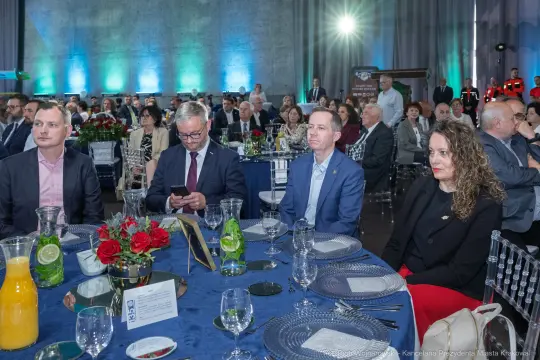 Uczestnicy wydarzenia siedzą przy elegancko nakrytych stołach w sali bankietowej.