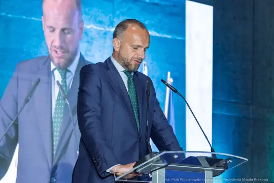 Mężczyzna w garniturze przemawia z mównicy podczas wydarzenia.