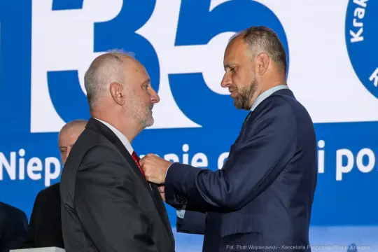 Wręczenie odznaczenia przez jednego mężczyznę drugiemu podczas uroczystości.