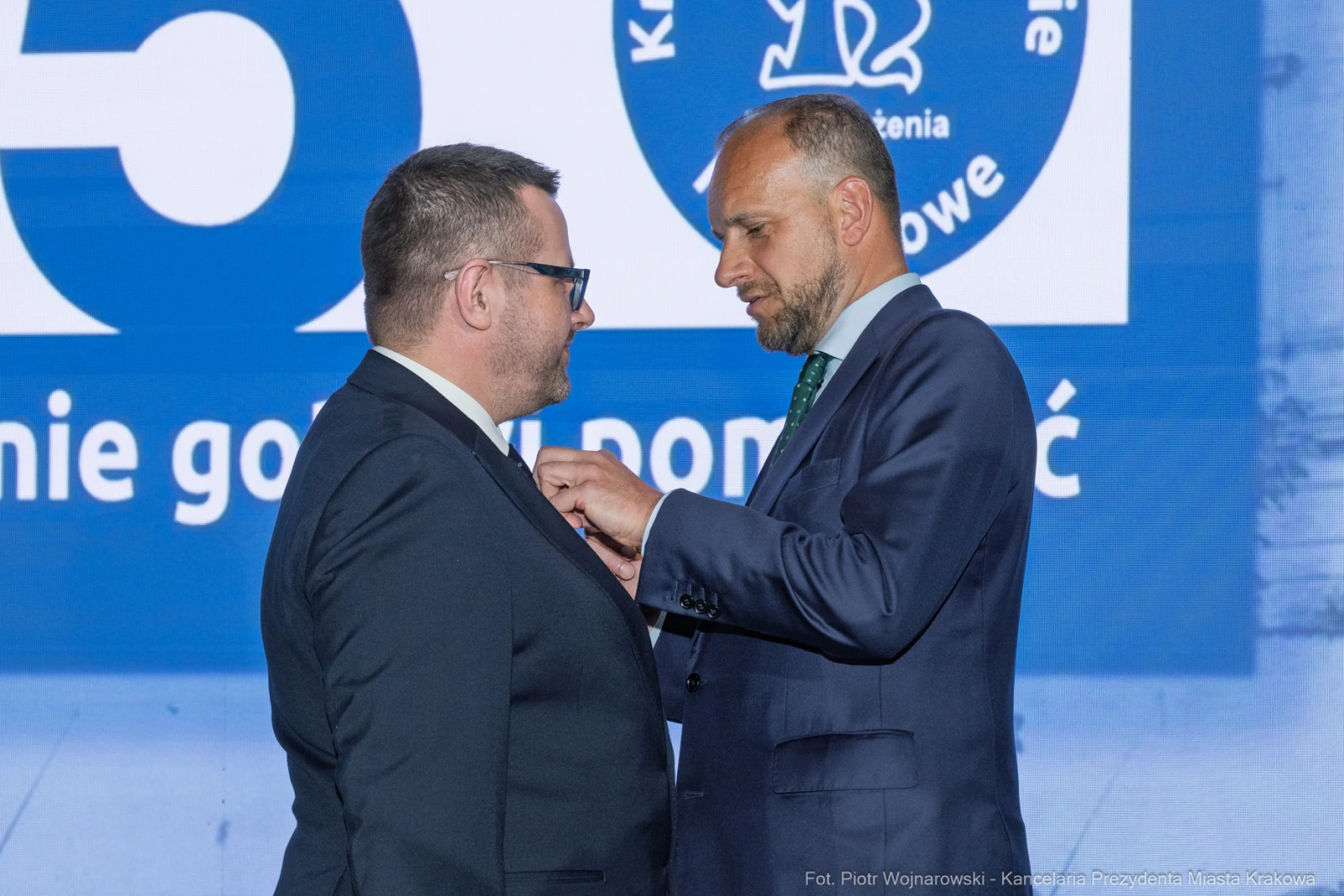 Mężczyzna przypina odznakę drugiemu mężczyźnie podczas uroczystości.  Autor: Piotr Wojnarowski