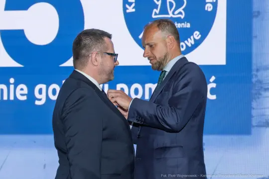Mężczyzna przypina odznakę drugiemu mężczyźnie podczas uroczystości.