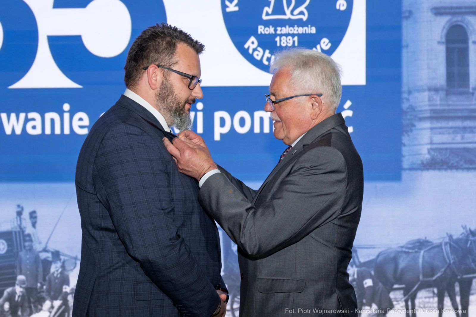 Uroczystość wręczenia odznaczenia mężczyźnie w garniturze przez starszego mężczyznę.  Autor: Piotr Wojnarowski