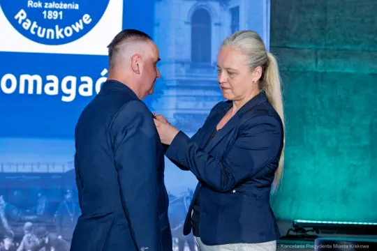 Wręczenie odznaczenia mężczyźnie przez kobietę podczas uroczystości.