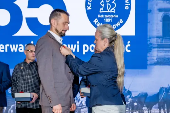 Mężczyzna odbiera odznaczenie od kobiety podczas uroczystości.