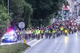 Grupa rowerzystów w kamizelkach odblaskowych na ulicy, towarzyszy im policyjny radiowóz.