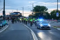 Grupa rowerzystów w kamizelkach odblaskowych jedzie obok policyjnego radiowozu.