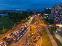 Ruch uliczny w mieście, z dużą ilością samochodów i pieszych w wieczornym świetle.