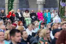 Grupa osób siedzących na widowni podczas wydarzenia, różnorodne stroje i wyraziste kolory.