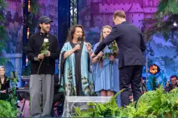 Czwórka ludzi na scenie, trzymają kwiaty, rozmawiają z prowadzącym.