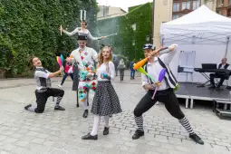 Grupa artystów cyrkowych w kolorowych strojach wykonuje sztuczki na ulicy.