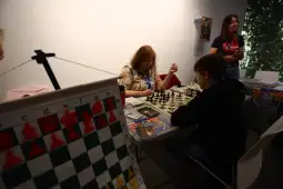Gra w szachy przy stole, uczestnicy skupieni na rozgrywce.