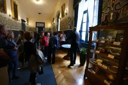 Grupa ludzi zwiedzająca muzeum, eksponaty w witrynach, dekoracyjne ściany.