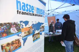 Stoisko informacyjne o misjach franciszkańskich z mapą świata i zdjęciami z działalności.