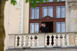 Mężczyzna w mundurze gra na trąbce z balkonu budynku.