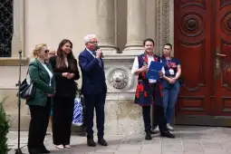 Cztery osoby na tle budynku, jedna z nich przemawia, pozostałe słuchają.