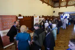 Tłum ludzi rozmawiających z przedstawicielem na stoisku informacyjnym.