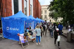 Targi z niebieskimi namiotami w Krakowie, ludzie spacerujący i oglądający stoiska.