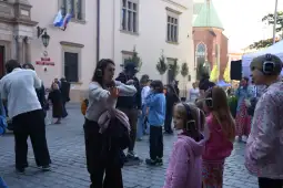Ludzie w słuchawkach bawią się na ulicy, w tle budynki i drzewa.