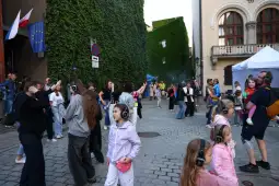 Uczestnicy imprezy tanecznej w słuchawkach na ulicy, otoczeni zielonymi ścianami.