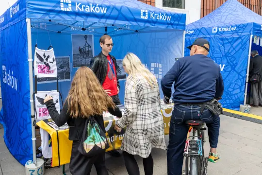 Stoisko promocyjne w Krakowie z osobą obsługującą i odwiedzającymi.
