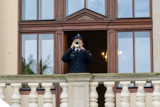 Mężczyzna w mundurze gra na trąbce z balkonu.