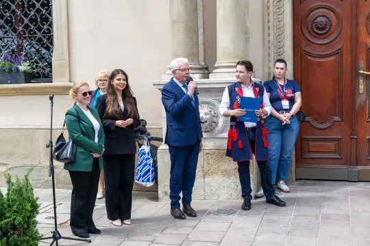 Ceremonia z mówcami i gośćmi na tle zabytkowej architektury.