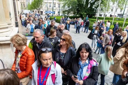 Ludzie stoją w kolejce przed budynkiem, czekając na wejście.
