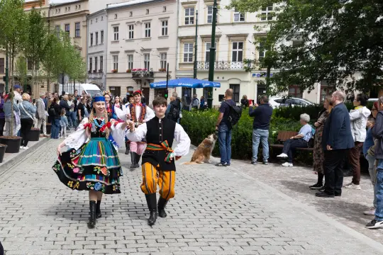 Dzieci w tradycyjnych strojach ludowych tańczą na ulicy, wokół tłum widzów.