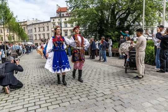 Para w tradycyjnych strojach ludowych tańczy na ulicy, otoczona widzami.