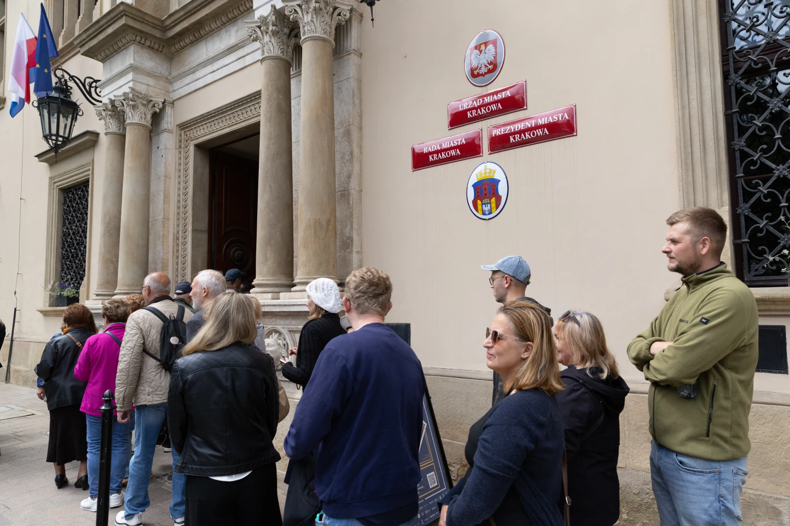 Kolejka ludzi przed budynkiem z herbami Krakowa i tablicami informacyjnymi.  Autor: Bogusław Świerzowski