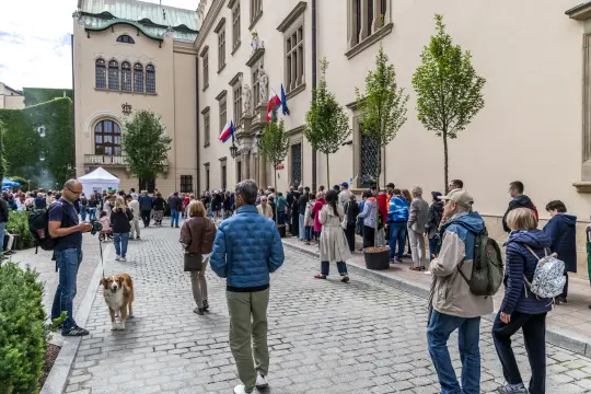 Tłum ludzi czekających w kolejce przed budynkiem z flagami.