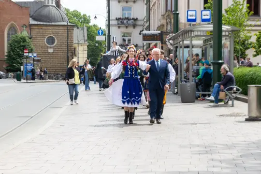 Grupa osób w tradycyjnych strojach ludowych spaceruje po ulicy.