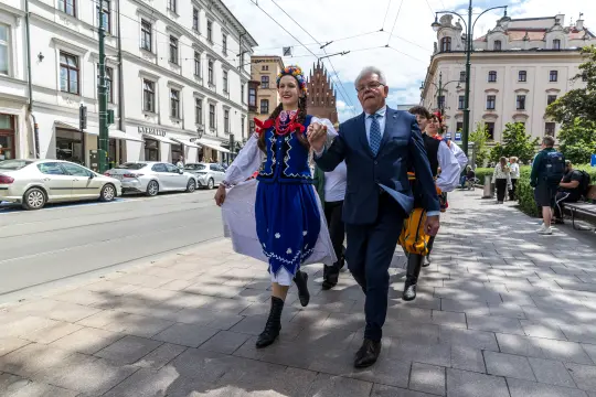 Kobieta w tradycyjnym stroju ludowym tańczy z mężczyzną w garniturze na ulicy.