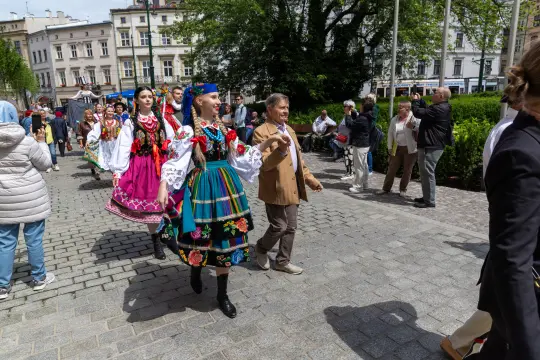 Grupa osób w tradycyjnych strojach ludowych tańczy na ulicy podczas festiwalu.