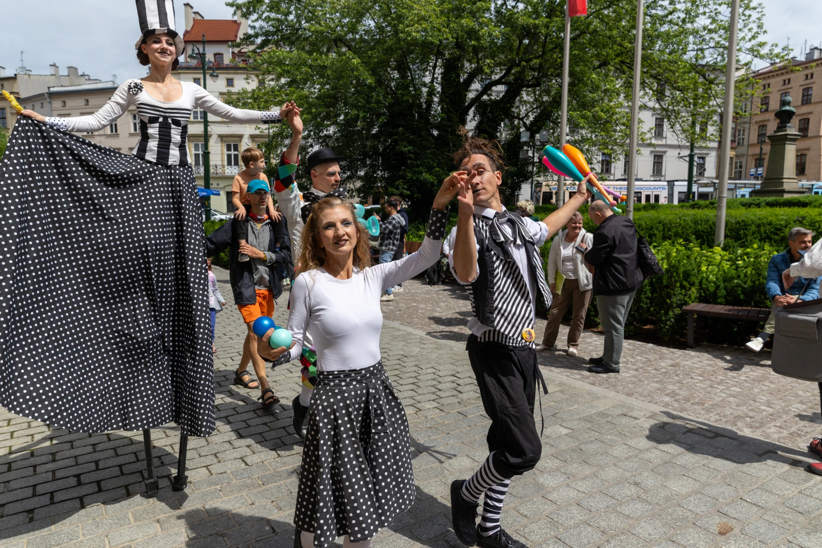 Grupa artystów ulicznych w kostiumach w paski i kropki, tańczących i bawiących się z publicznością.  Autor: Bogusław Świerzowski