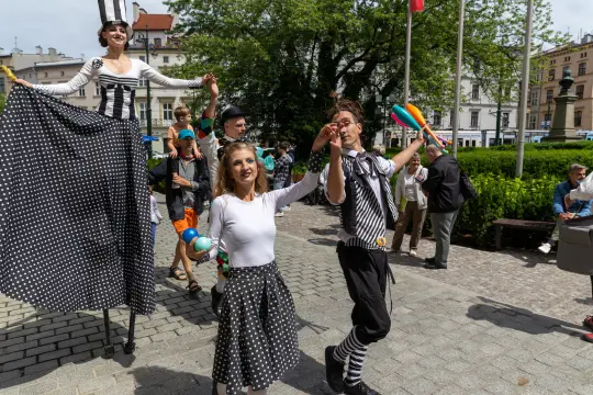 Grupa artystów ulicznych w kostiumach w paski i kropki, tańczących i bawiących się z publicznością.