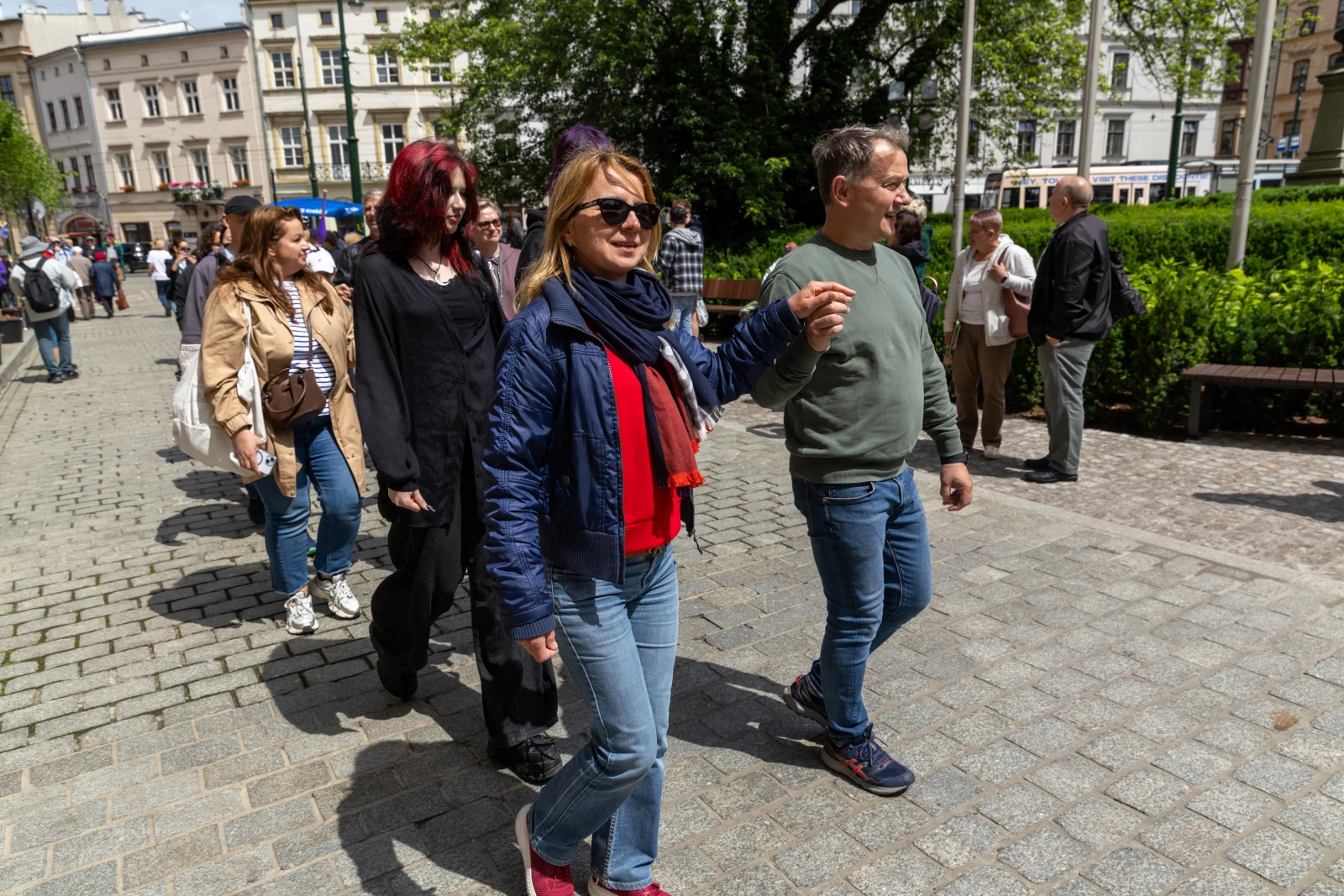 Grupa ludzi spacerujących po miejskiej ulicy w słoneczny dzień.  Autor: Bogusław Świerzowski